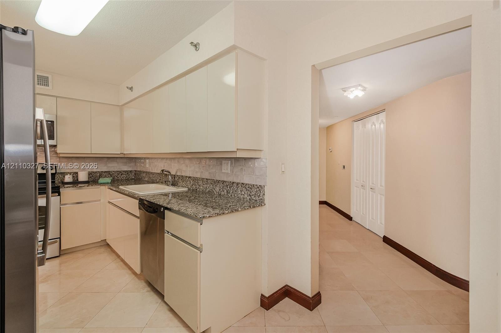 Kitchen featuring flat-panel cabinetry, light-toned stone countertops, a dark-finish double-door refrigerator, and polished stone tile flooring throug