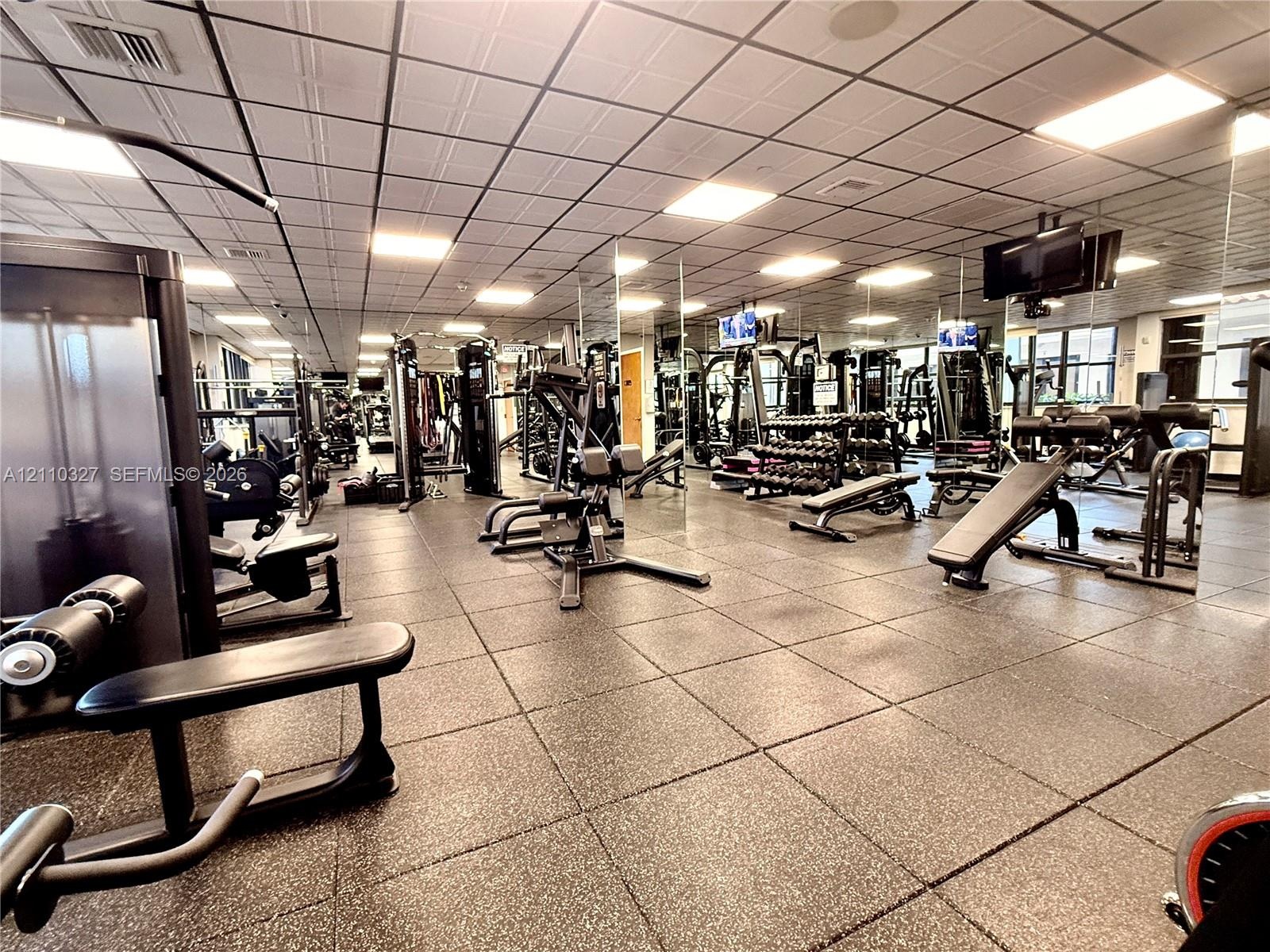 Fitness area featuring a coffered drop ceiling, expansive wall-to-wall mirrors, and durable rubberized flooring