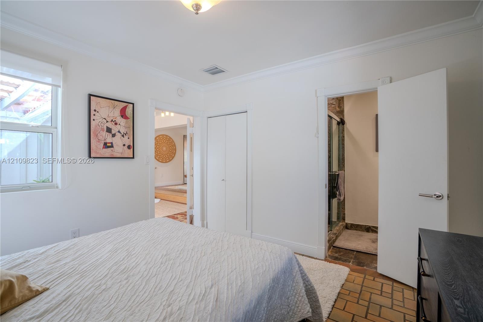 Neutral wall palette with crown molding, double-door closet, terracotta-style tile flooring, and en suite bathroom featuring a glass-enclosed shower
