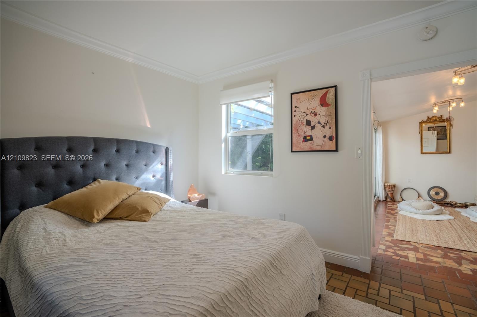 Neutral-toned room featuring crown molding, a window with a roller shade, and tile flooring