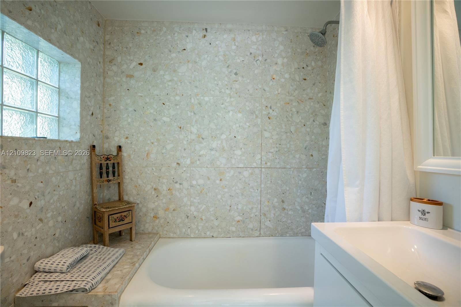 Bathroom featuring terrazzo wall tiles, a built-in tub surround, a glass block window, and a wall-mounted shower head