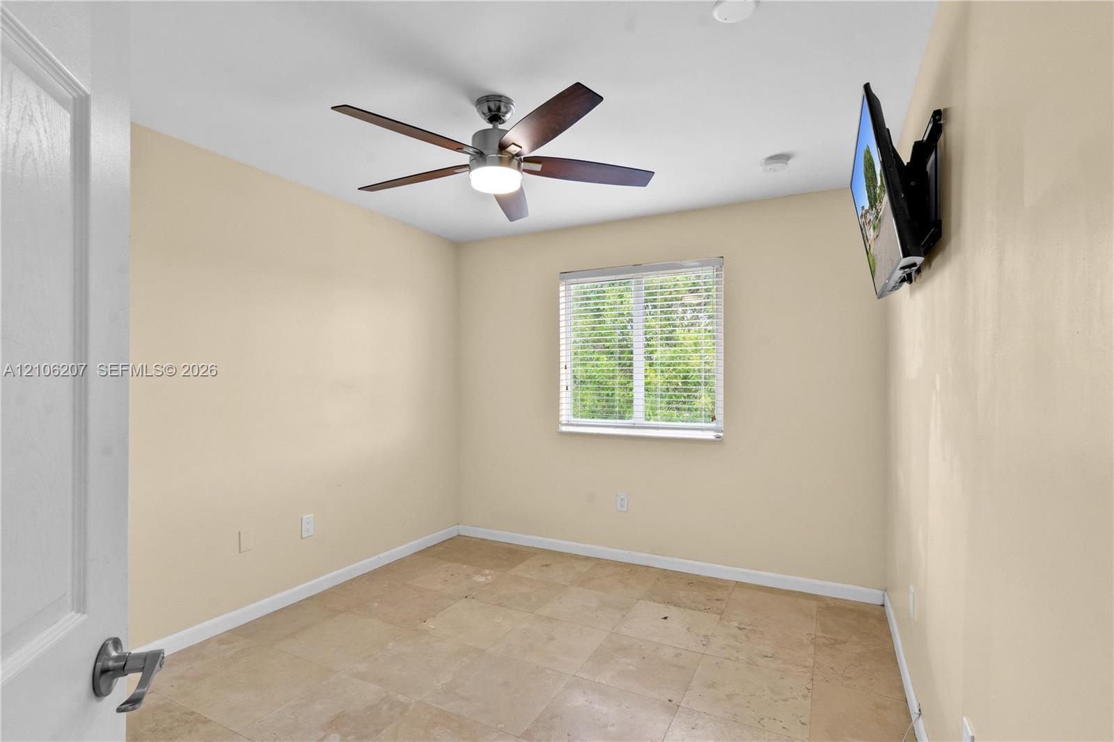 Neutral-toned room featuring stone-finish flooring, a five-blade ceiling fan with integrated lighting, and a window with horizontal blinds