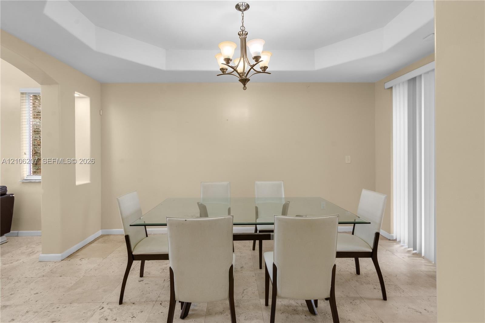 Tray ceiling with multi-arm chandelier, stone flooring, and built-in wall niche