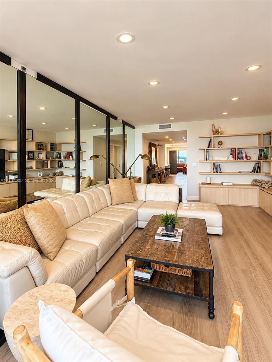 Wood-finish flooring, full-length mirror wall, recessed ceiling lighting, and built-in wood cabinetry with integrated shelving