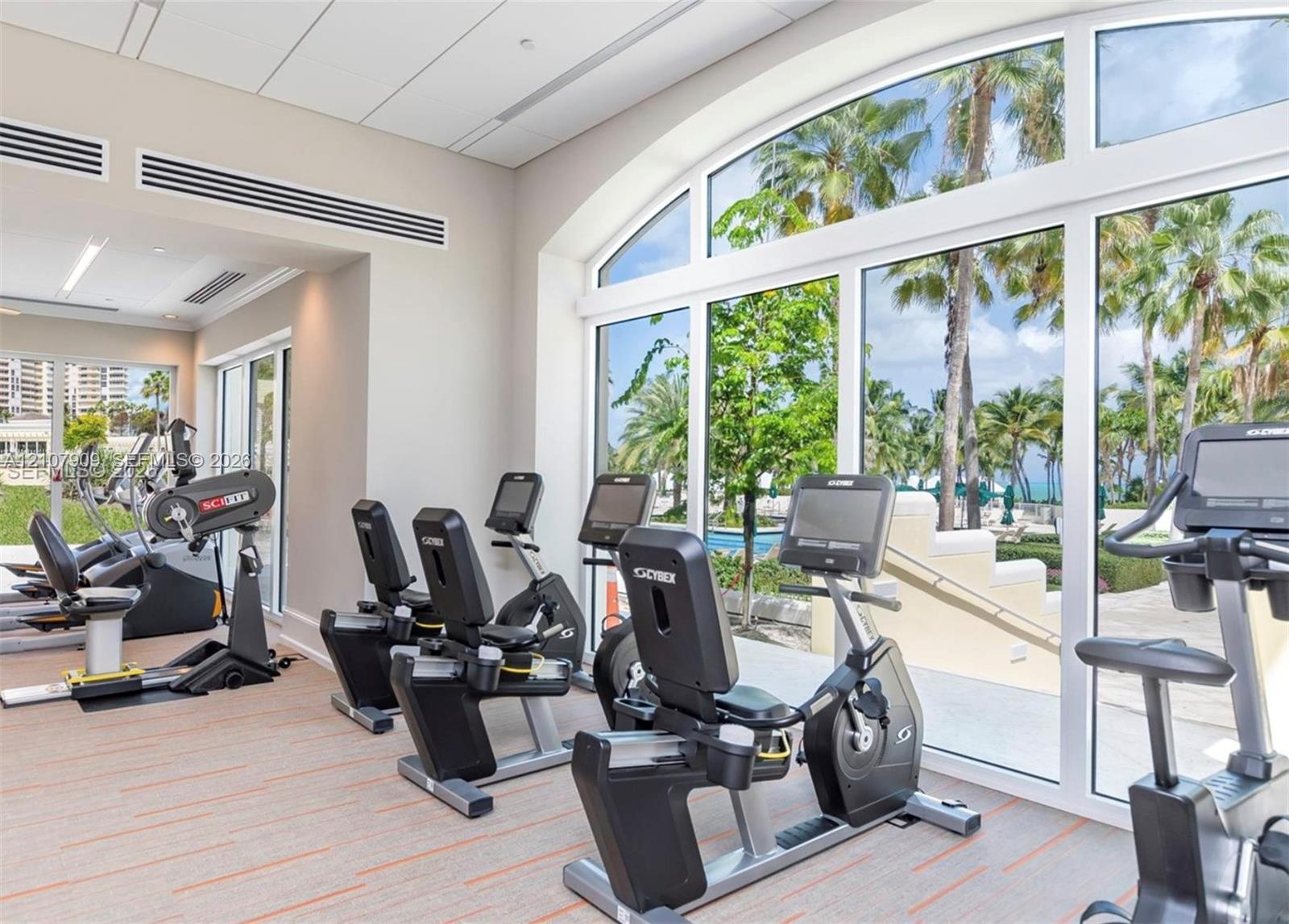 Fitness center featuring floor-to-ceiling arched windows, high-contrast light walls, and commercial-grade carpet tile flooring