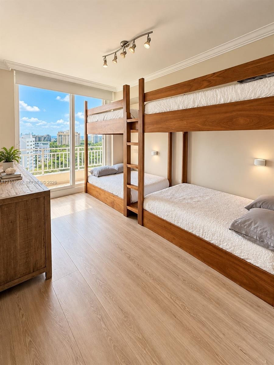 Floor-to-ceiling glass sliding door with balcony access, wood-finish flooring, crown molding, track lighting, and wall-mounted sconces