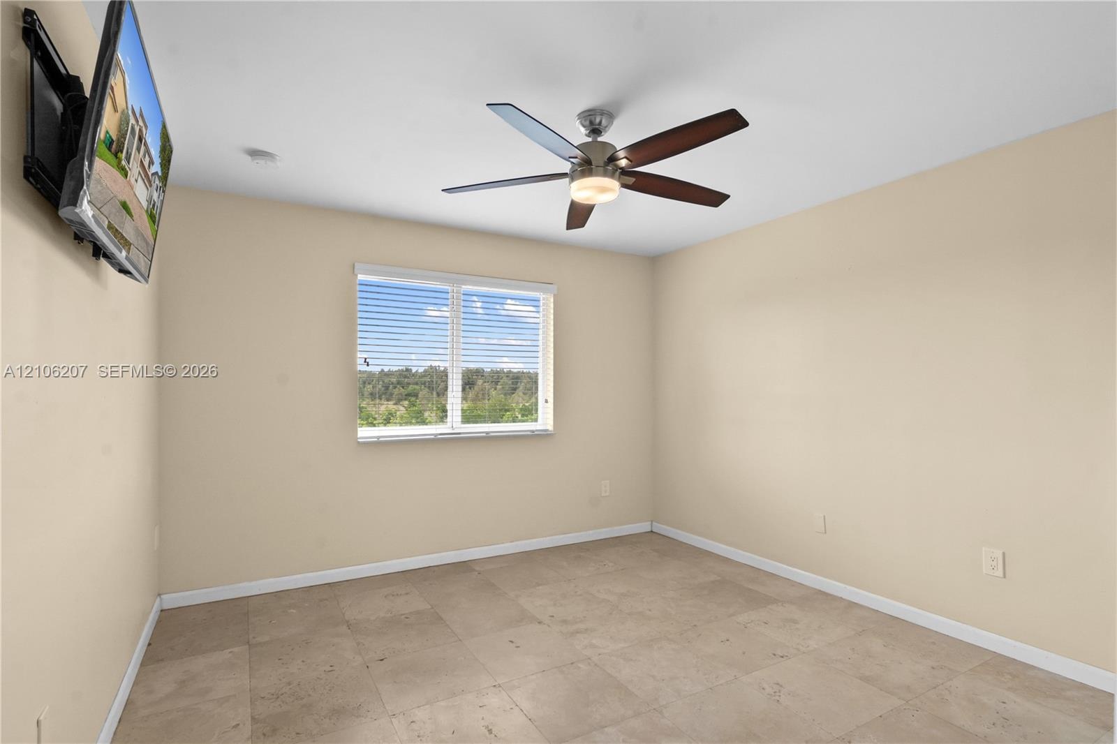 Room featuring large-format tile flooring, a multi-blade ceiling fan with an integrated light fixture, and a window with horizontal blinds