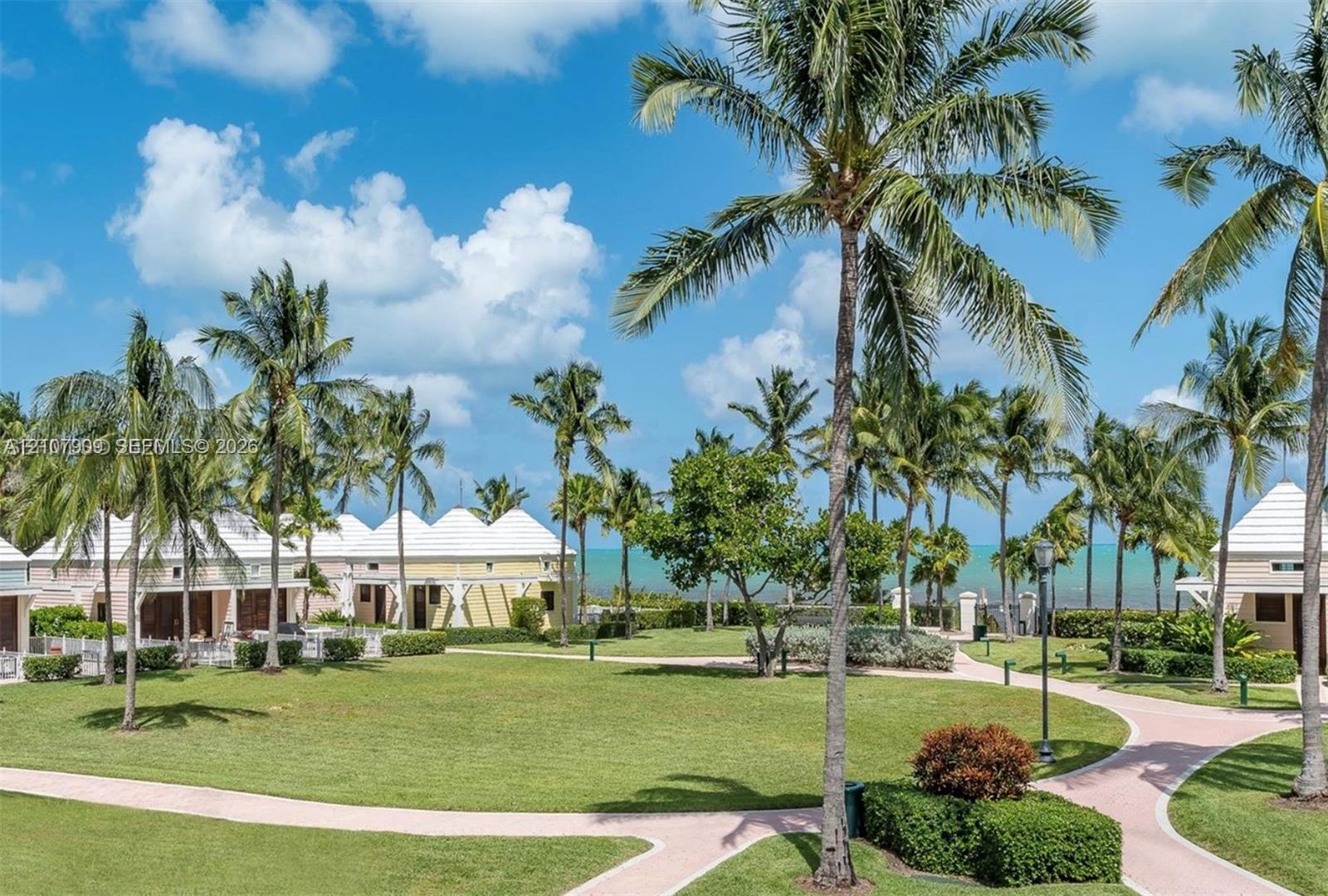 Landscaped grounds featuring mature palm trees, paved walkways, manicured lawn areas, and light-colored exterior structures with gabled roofs