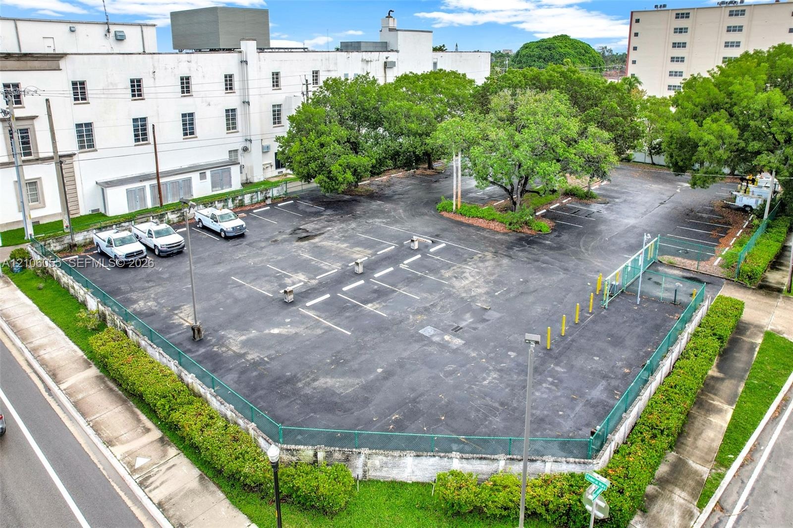 Asphalt-paved surface parking lot featuring perimeter chain-link fencing, painted parking stalls, and mature trees