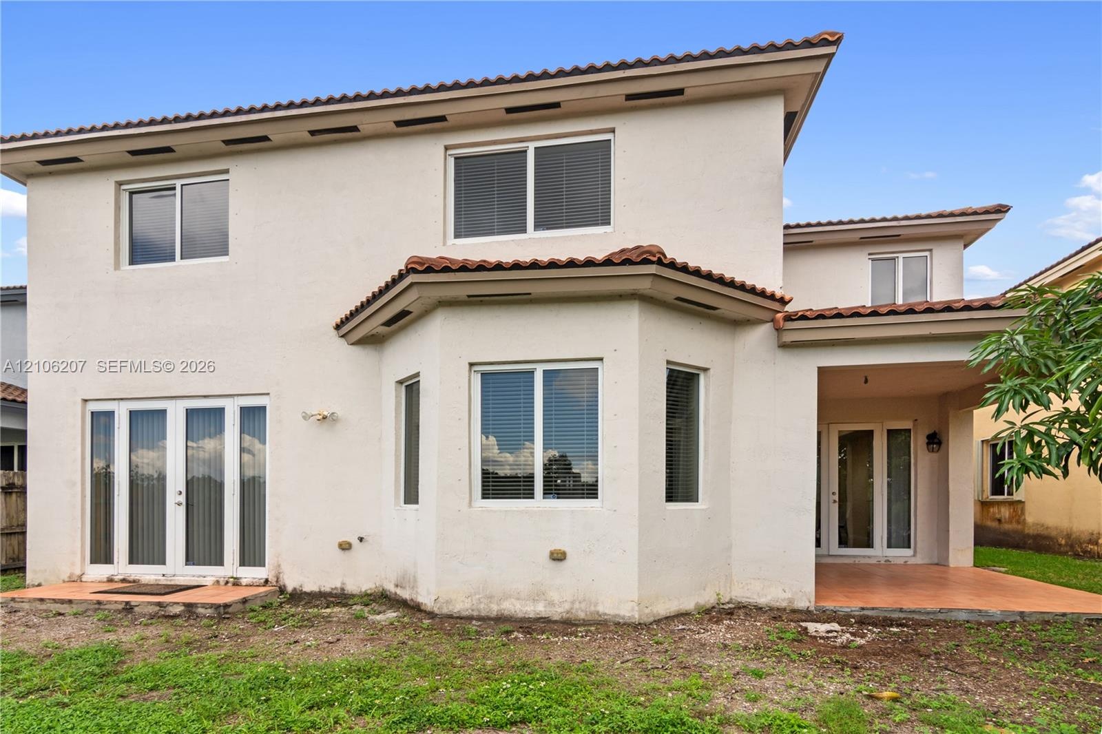 Stucco exterior residence featuring a multi-paneled bay window, tile-roofed overhangs, multiple sets of glass-paned doors, and a covered patio area