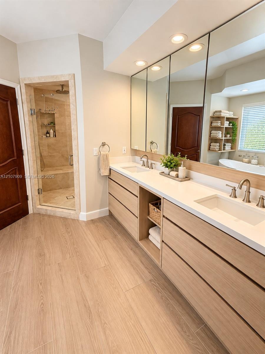 Dual-vanity cabinet featuring light-toned wood cabinetry, stone countertops, integrated under-mount sinks, and widespread faucets, complemented by a w