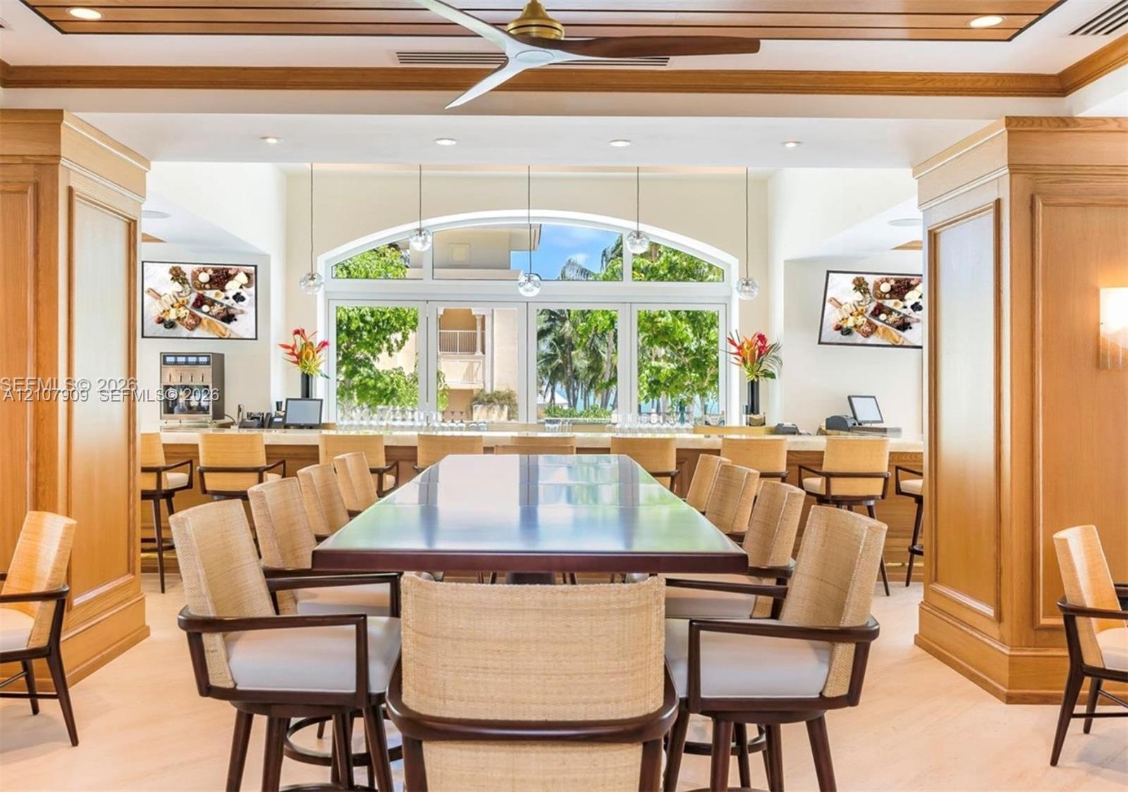 Custom wood-paneled walls and ceiling, large arched window, built-in service bar with stone countertop, ceiling fan with wood-finish blades, and reces