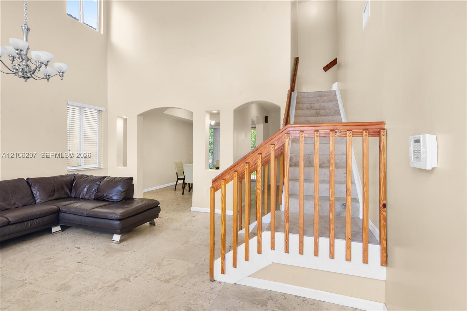Double-height ceilings featuring an arched wall opening, tile flooring, and a staircase with a wooden balustrade and carpeted treads