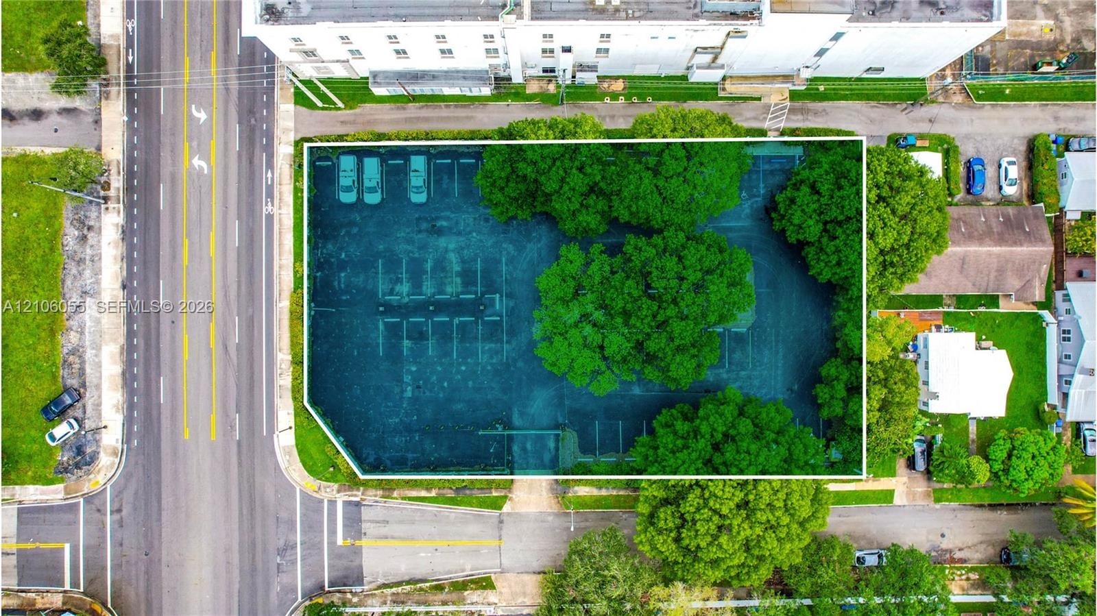 Aerial perspective of a corner lot featuring paved off-street parking, designated parking stalls, and mature trees providing shade
