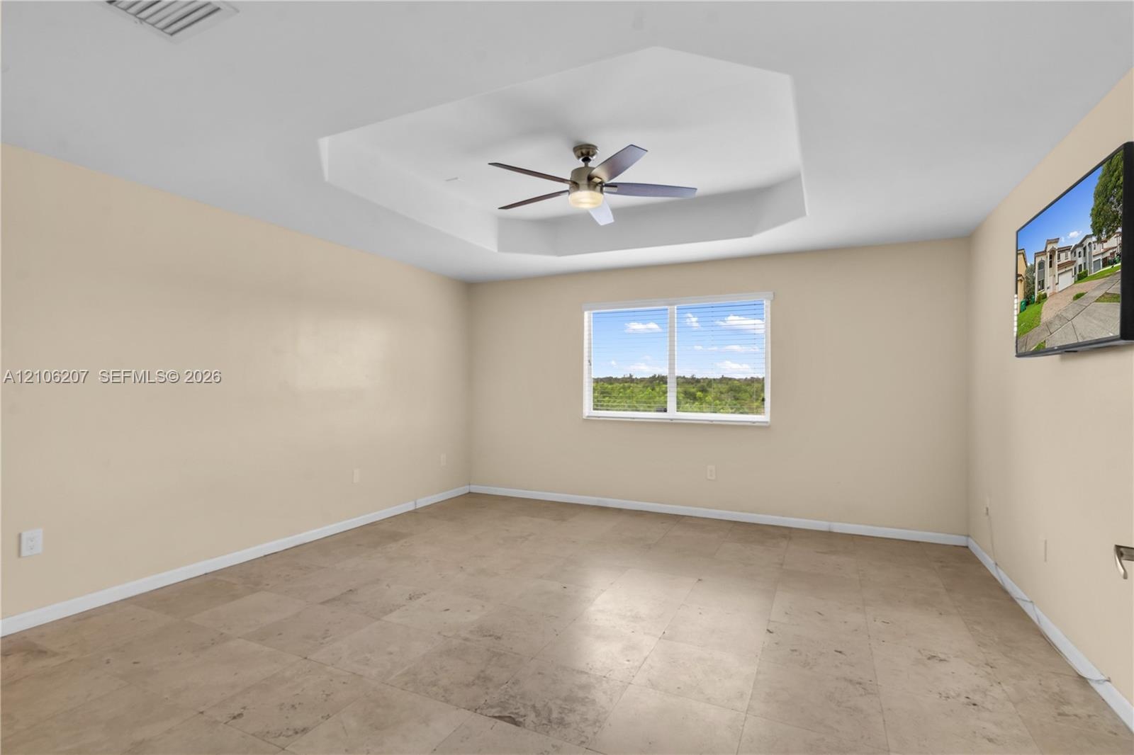 Interior room featuring a tray ceiling with a multi-blade ceiling fan and light fixture, stone-finish tile flooring, and a window with exterior landsc
