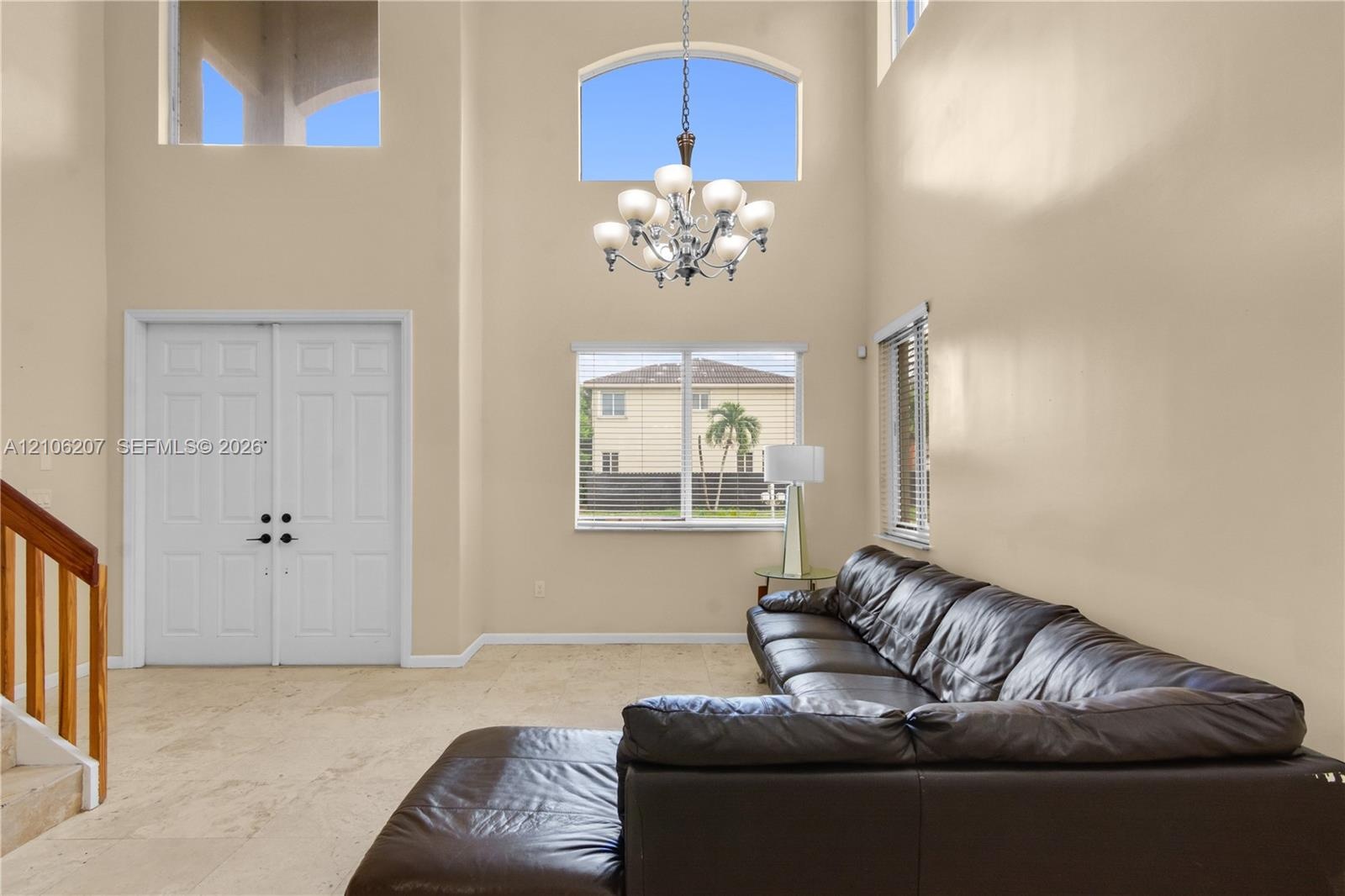 Double-height ceilings, arched transom windows, tile flooring, multi-light chandelier, and double-door entry