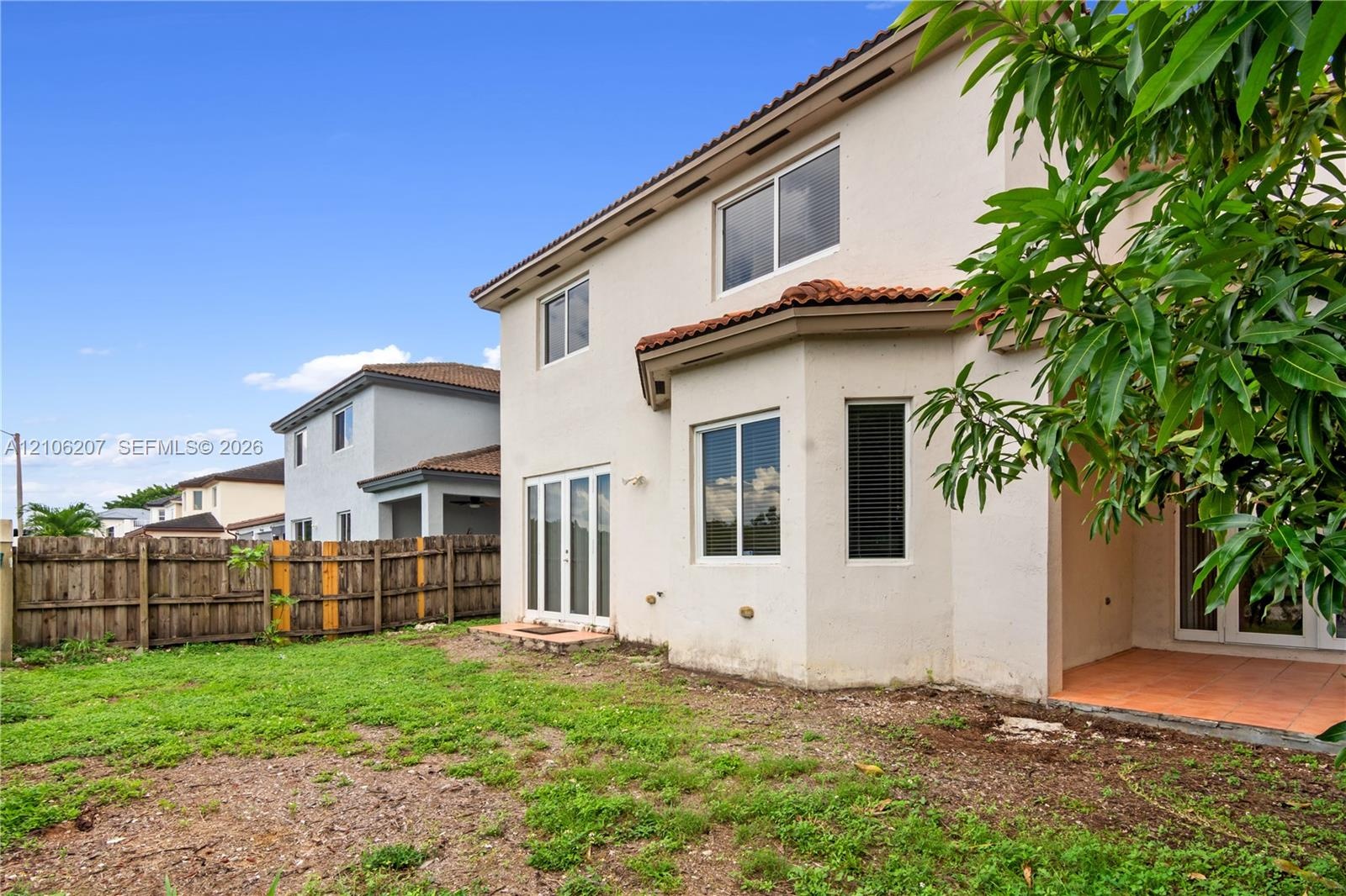 Rear exterior featuring a two-story stucco facade, tiled roof, covered patio, glass sliding doors, and wood-panel fencing