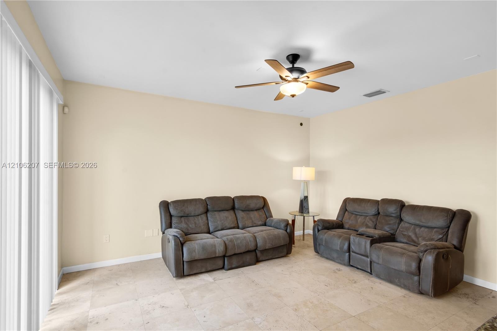 Neutral-toned living space featuring large-format tile flooring, a central ceiling fan with integrated lighting, and full-height sliding glass doors