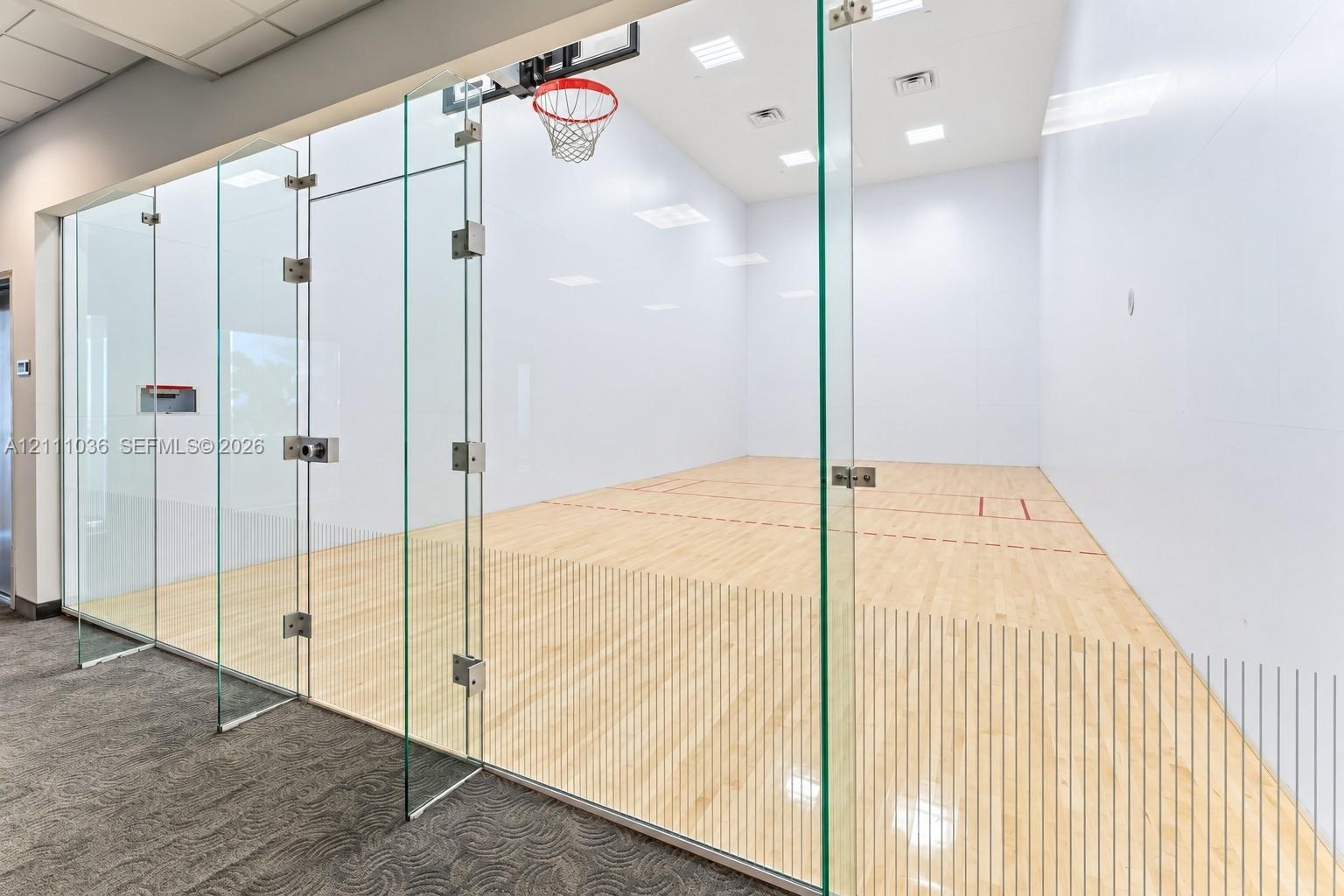 Recreational court featuring frameless glass wall enclosures, high-contrast wood-finish flooring, recessed ceiling lighting, and a built-in basketball