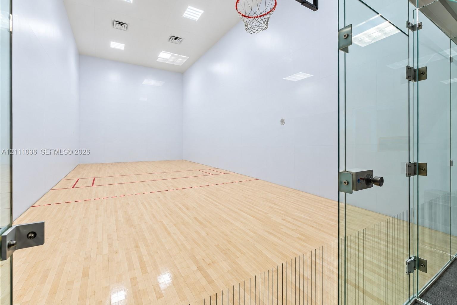 Recreational court featuring wood-finish flooring, high-impact walls, glass enclosure, and overhead recessed lighting