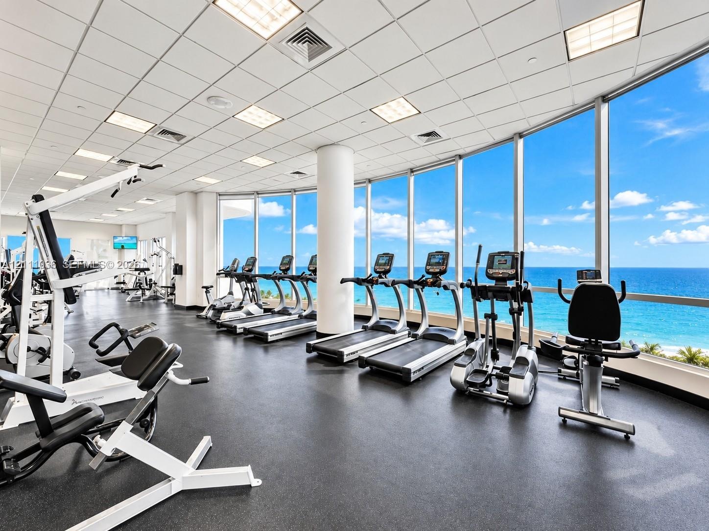 Fitness center featuring floor-to-ceiling windows, panoramic ocean scenery, recessed lighting, and rubberized flooring