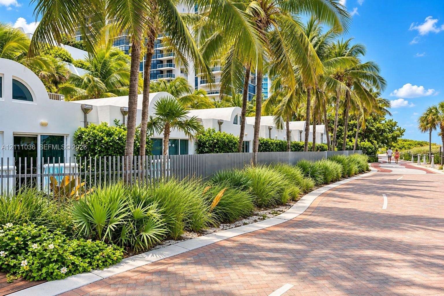 Stucco exterior featuring arched rooflines, integrated metal fencing, mature palm trees, and native ornamental landscaping situated along a paved bric