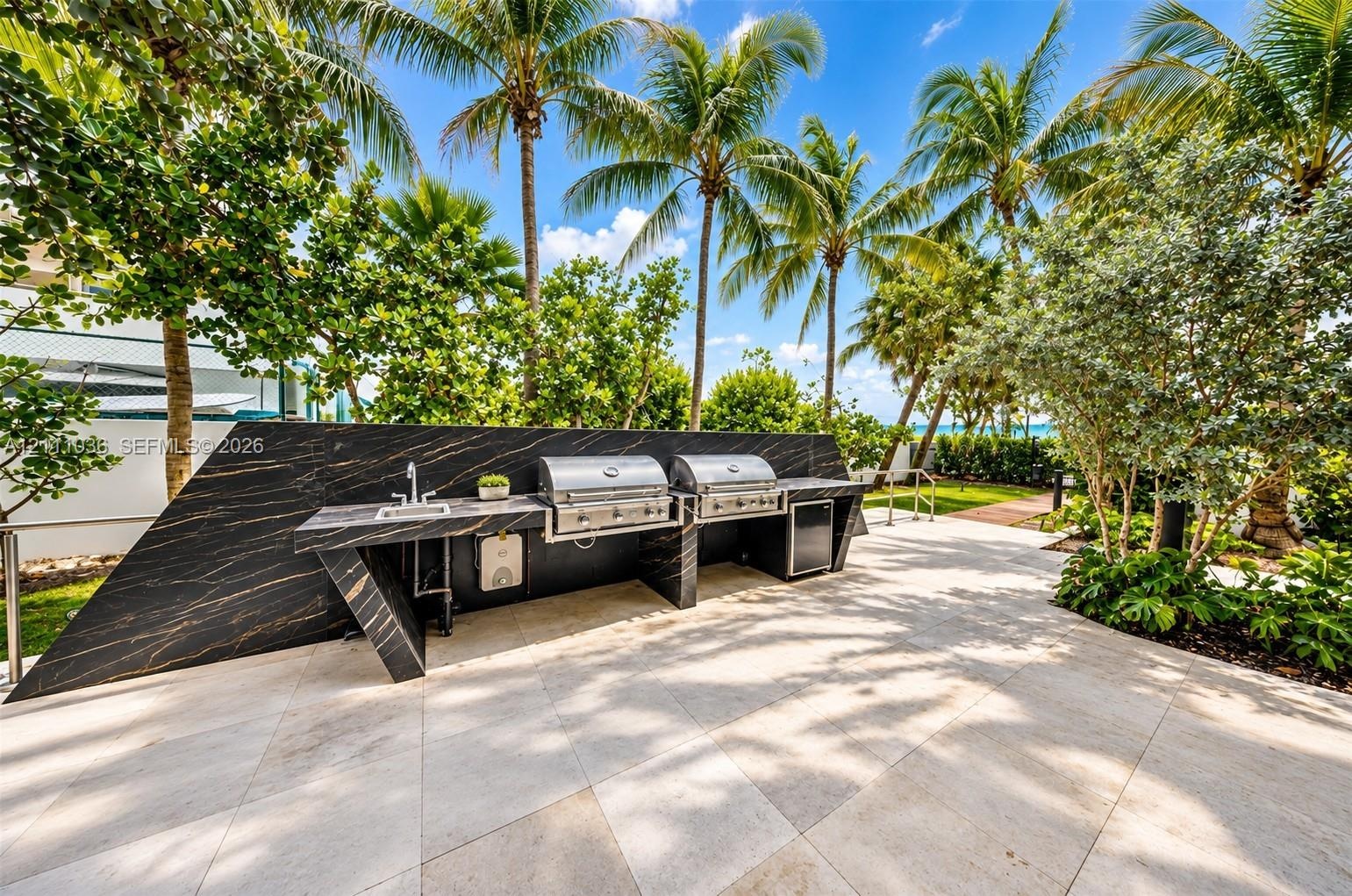 Outdoor kitchen featuring a sleek, dark-veined stone countertop, built-in stainless steel dual grills, an integrated stainless steel sink, and light-t