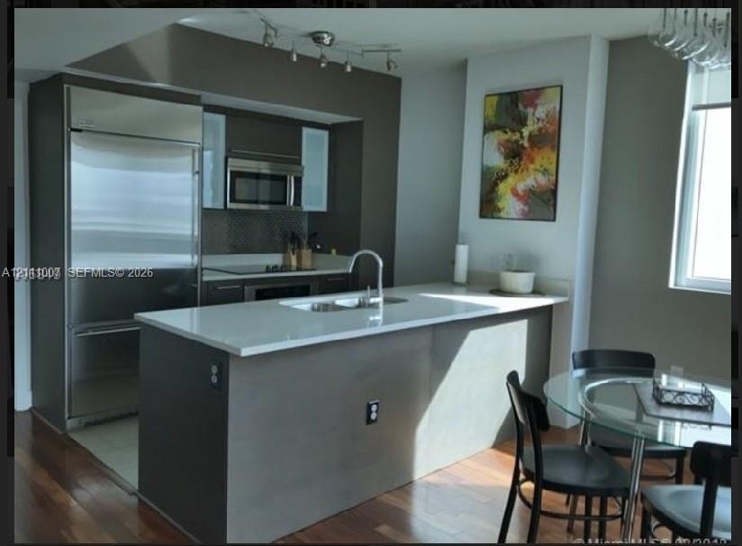 Kitchen featuring an island with a quartz countertop, stainless steel refrigerator, built-in microwave, track lighting, and wood-finish flooring