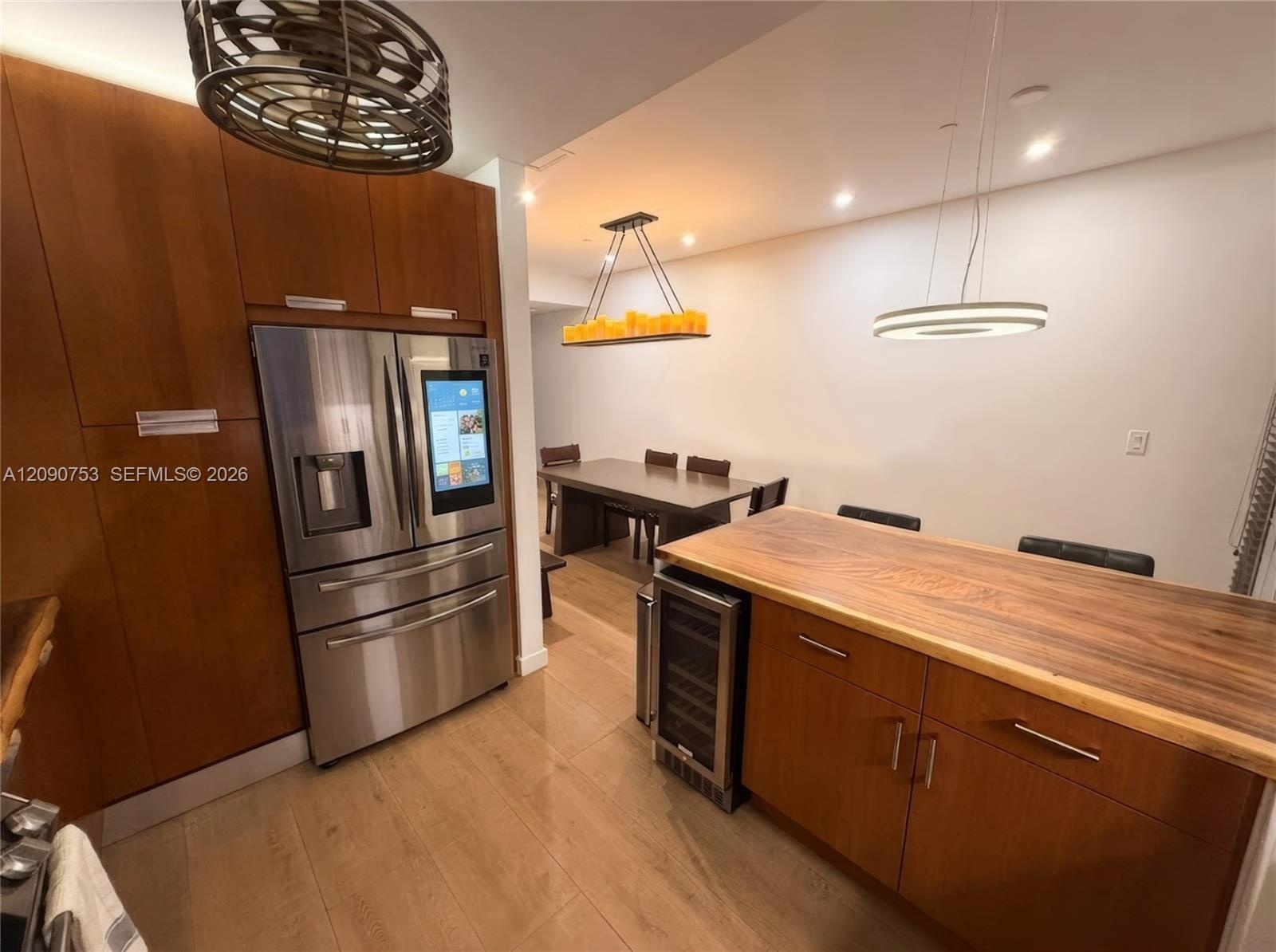 Kitchen featuring wood-veneer cabinetry, integrated stainless steel refrigerator, wood-slab island countertop, built-in wine cooler, and decorative li