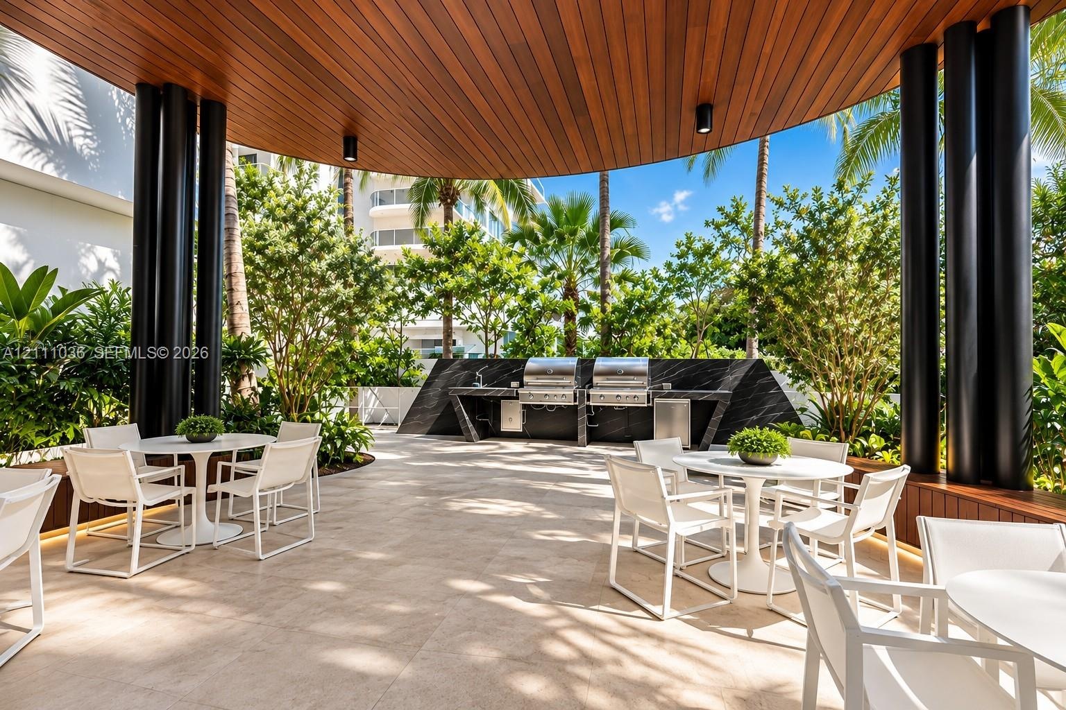Covered outdoor kitchen featuring dual stainless steel grills, stone-finish countertops, wood-paneled ceiling, and large-format tile flooring