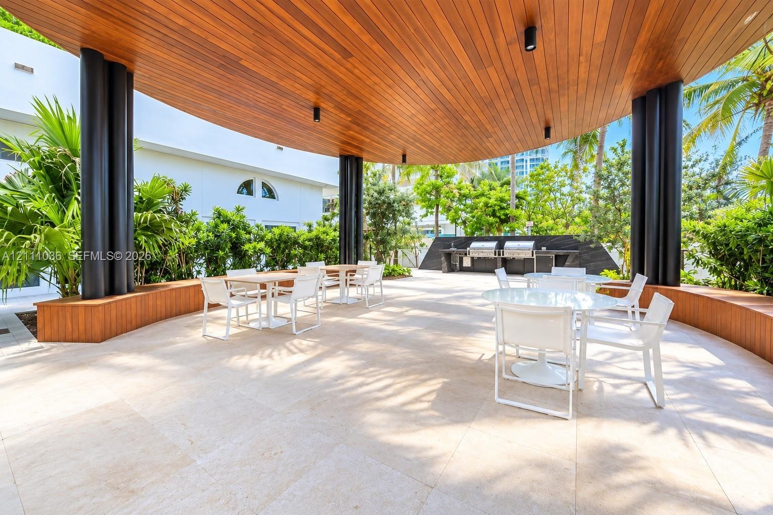 Covered outdoor terrace featuring a wood-paneled ceiling, stone tile flooring, structural cylindrical columns, and a built-in outdoor kitchen station 