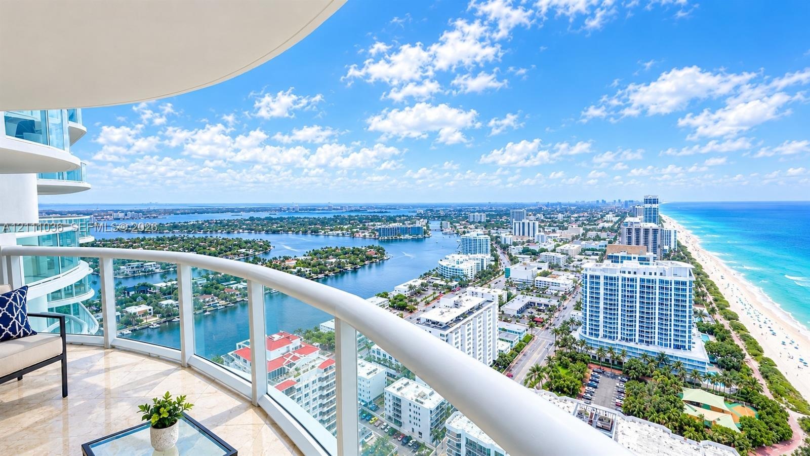 Curved covered balcony featuring stone flooring and glass-panel railings with expansive coastal and cityscape scenery
