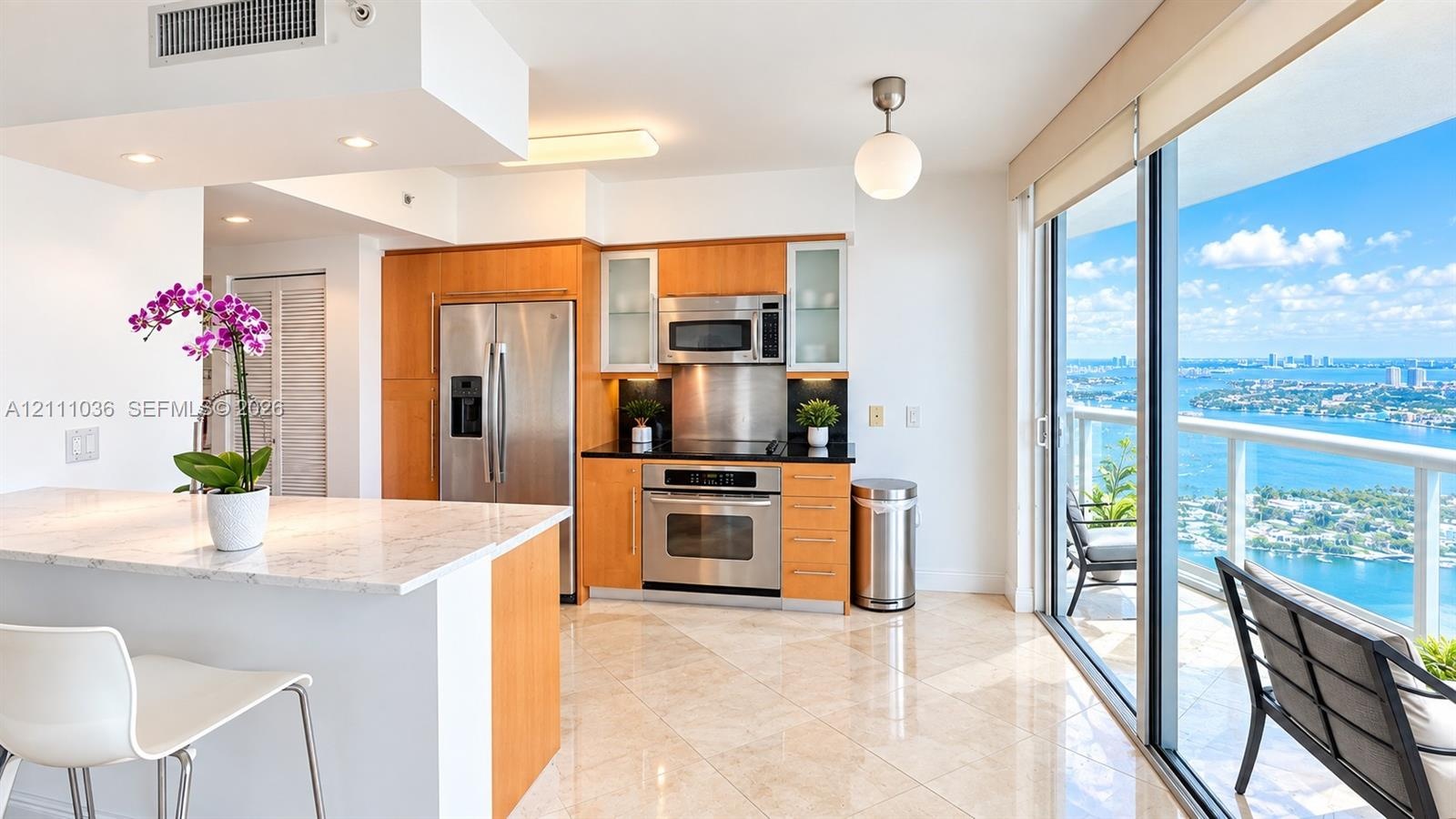 Kitchen featuring wood-finish cabinetry, stainless steel appliances, stone-topped island, polished tile flooring, and floor-to-ceiling glass sliding d