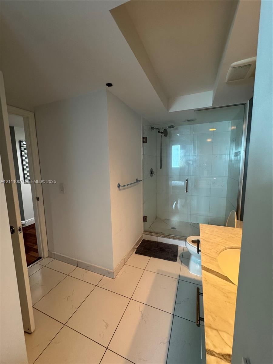 Walk-in glass enclosed shower with a polished metal faucet, white ceramic tile flooring, and a stone-surface vanity with an integrated sink