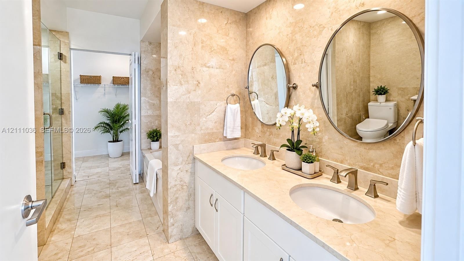 Double vanity featuring white cabinetry, stone-finish countertops, dual oval mirrors, and wall-mounted metallic fixtures, accented by floor-to-ceiling