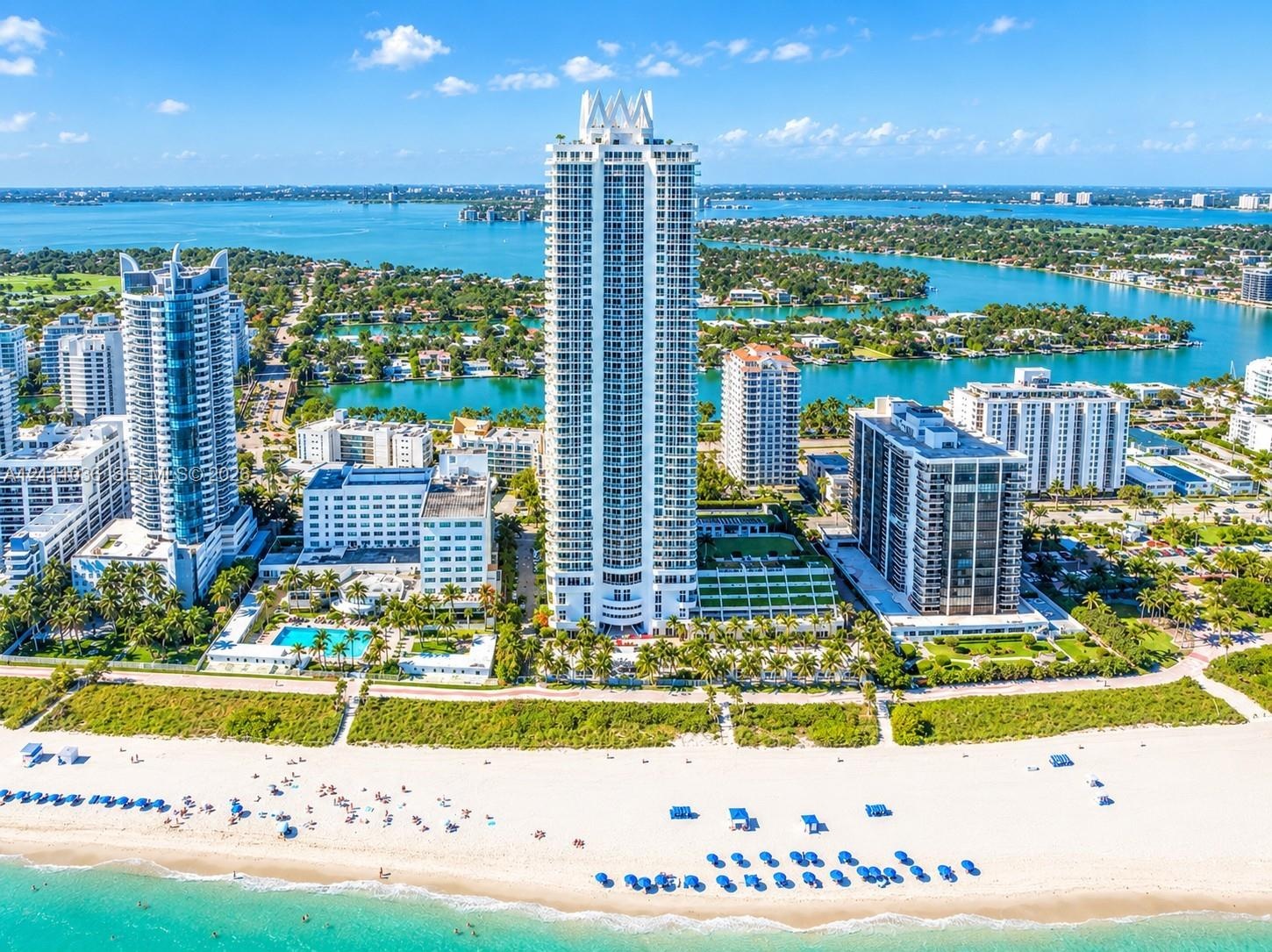 High-rise residential tower featuring a white concrete exterior, tiered architectural design, expansive glass balcony railings, direct sand beach acce