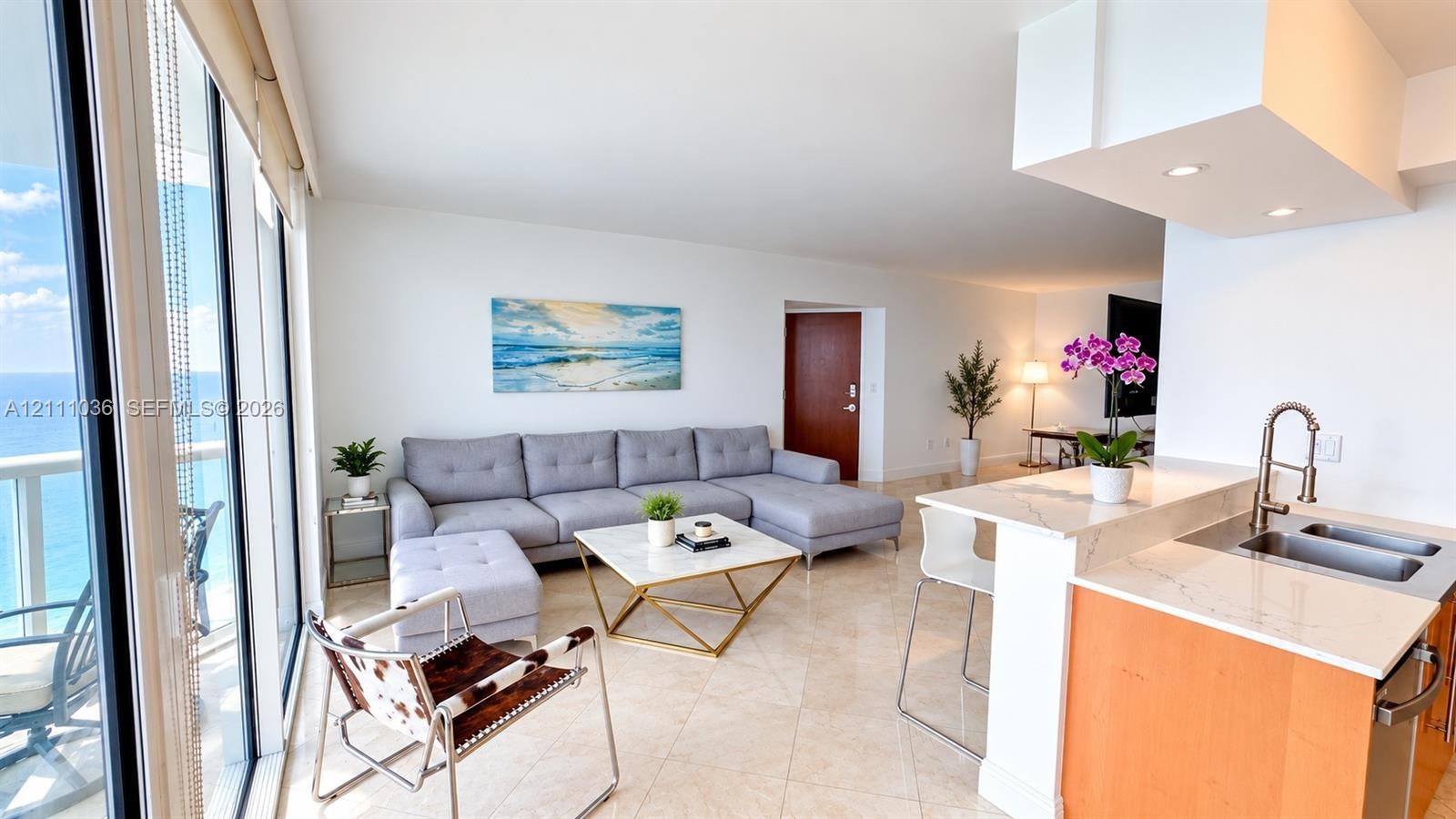Open-concept living space featuring floor-to-ceiling windows, natural stone flooring, kitchen peninsula with a quartz countertop, and recessed lightin
