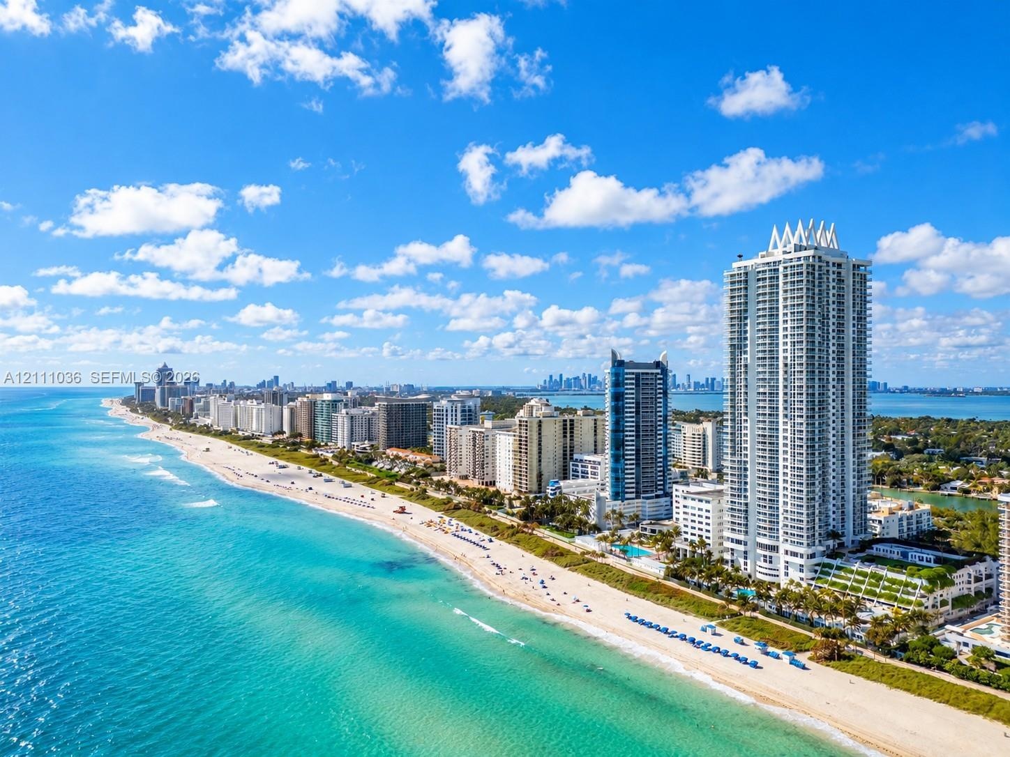 High-rise coastal tower featuring a white concrete facade, expansive glass balconies, direct beachfront access, and a multi-level terraced podium