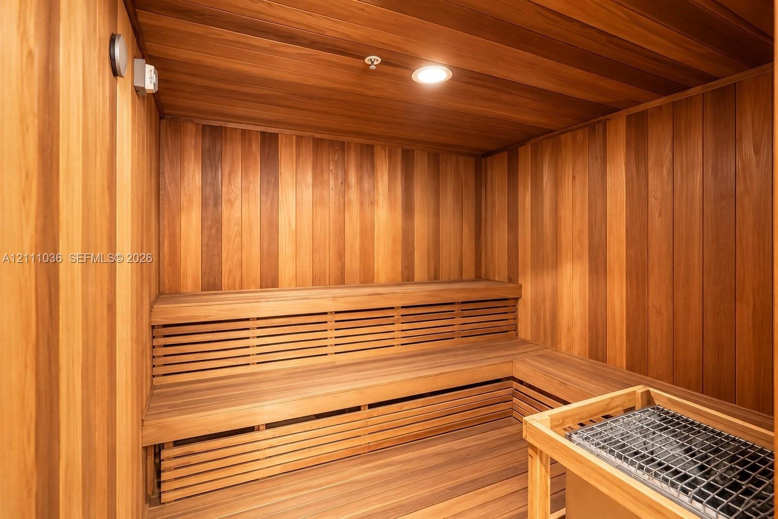 Sauna featuring tongue-and-groove wood paneling, multi-level built-in bench seating, recessed ceiling lighting, and a stone-filled heating unit with a