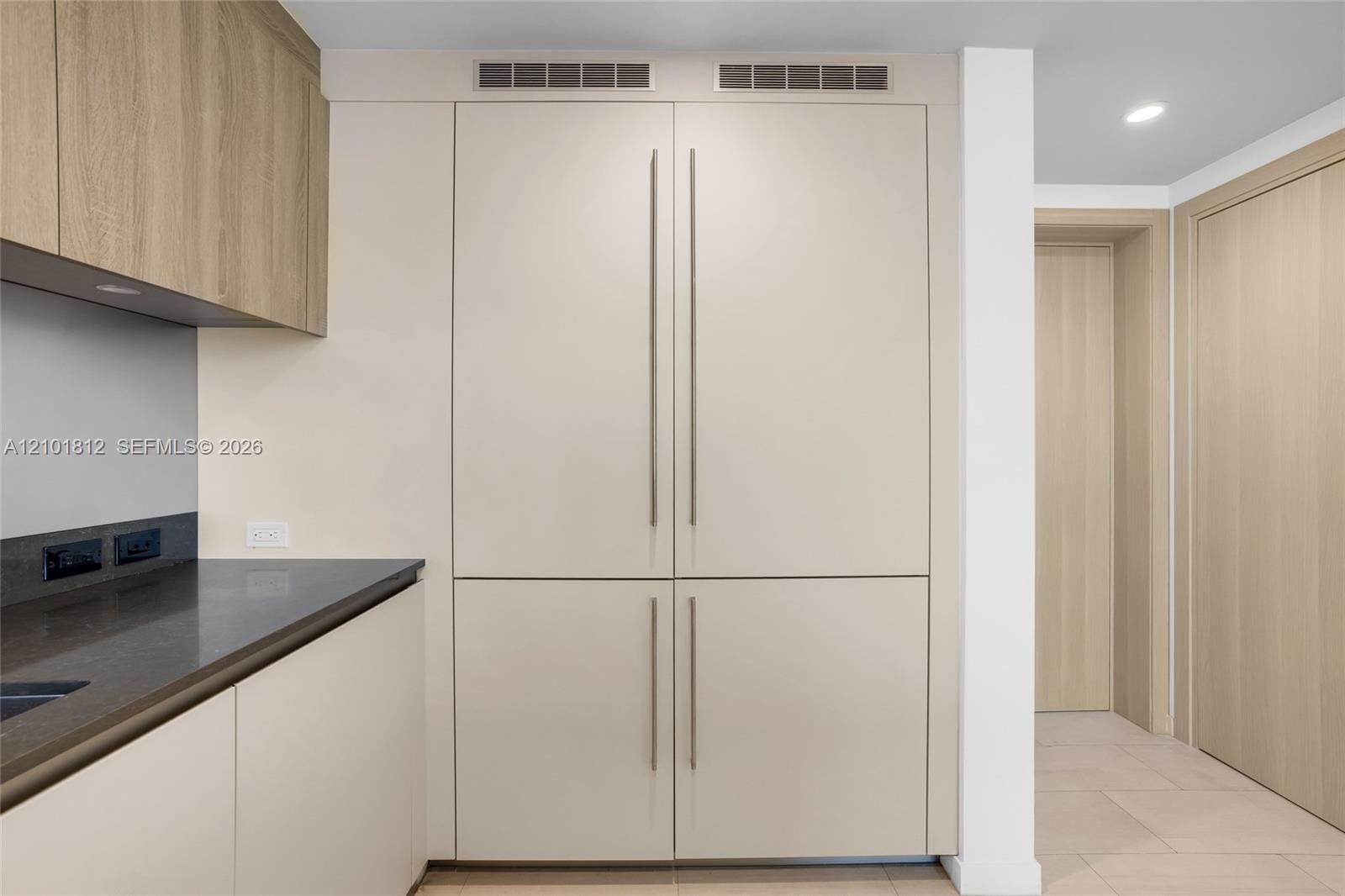 Built-in floor-to-ceiling cabinetry with matte finish, light wood-finish upper cabinets, dark solid surface countertop, and integrated panel-ready app
