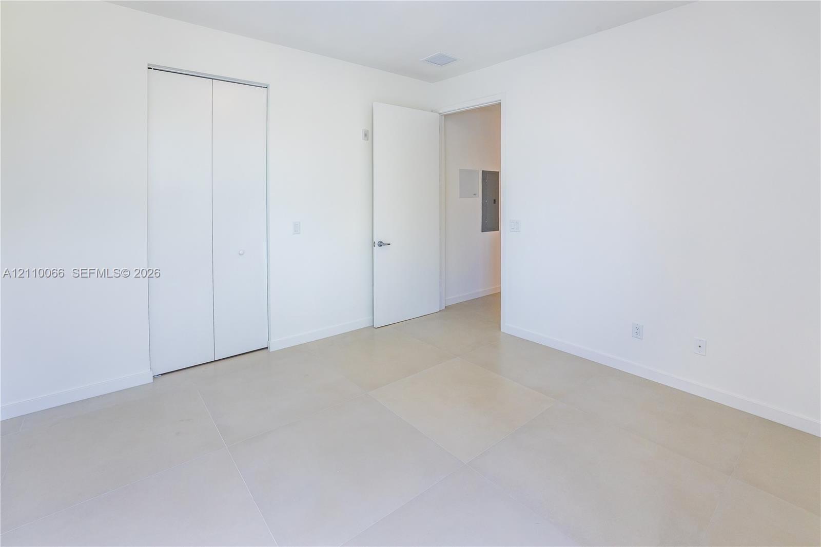 Neutral interior space featuring large-format tile flooring, a dual-panel closet with brushed nickel hardware, and a solid-core interior door