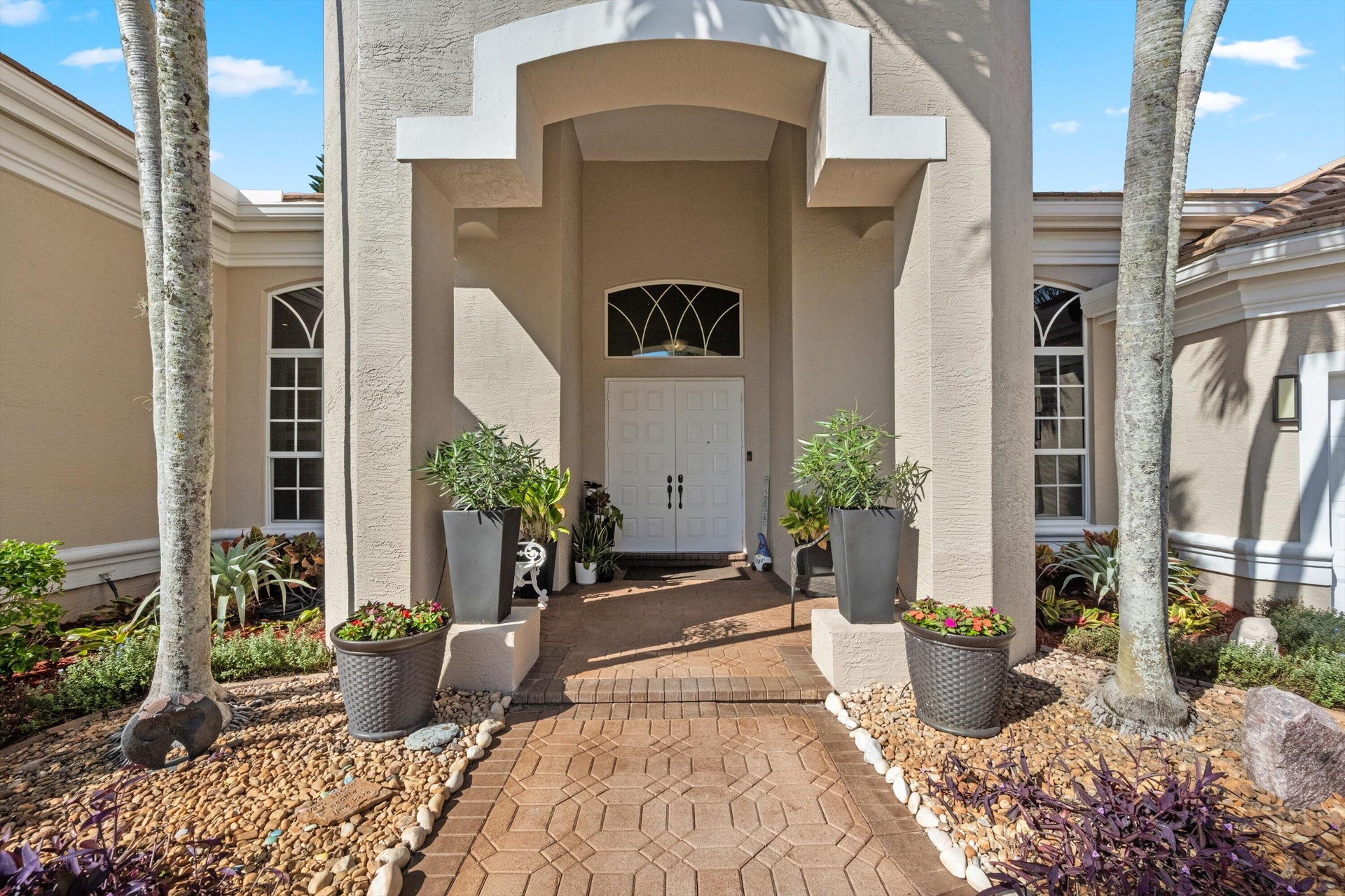 Stucco exterior featuring a covered entryway with arched transom window, dual-paneled entry doors, and patterned paver walkway