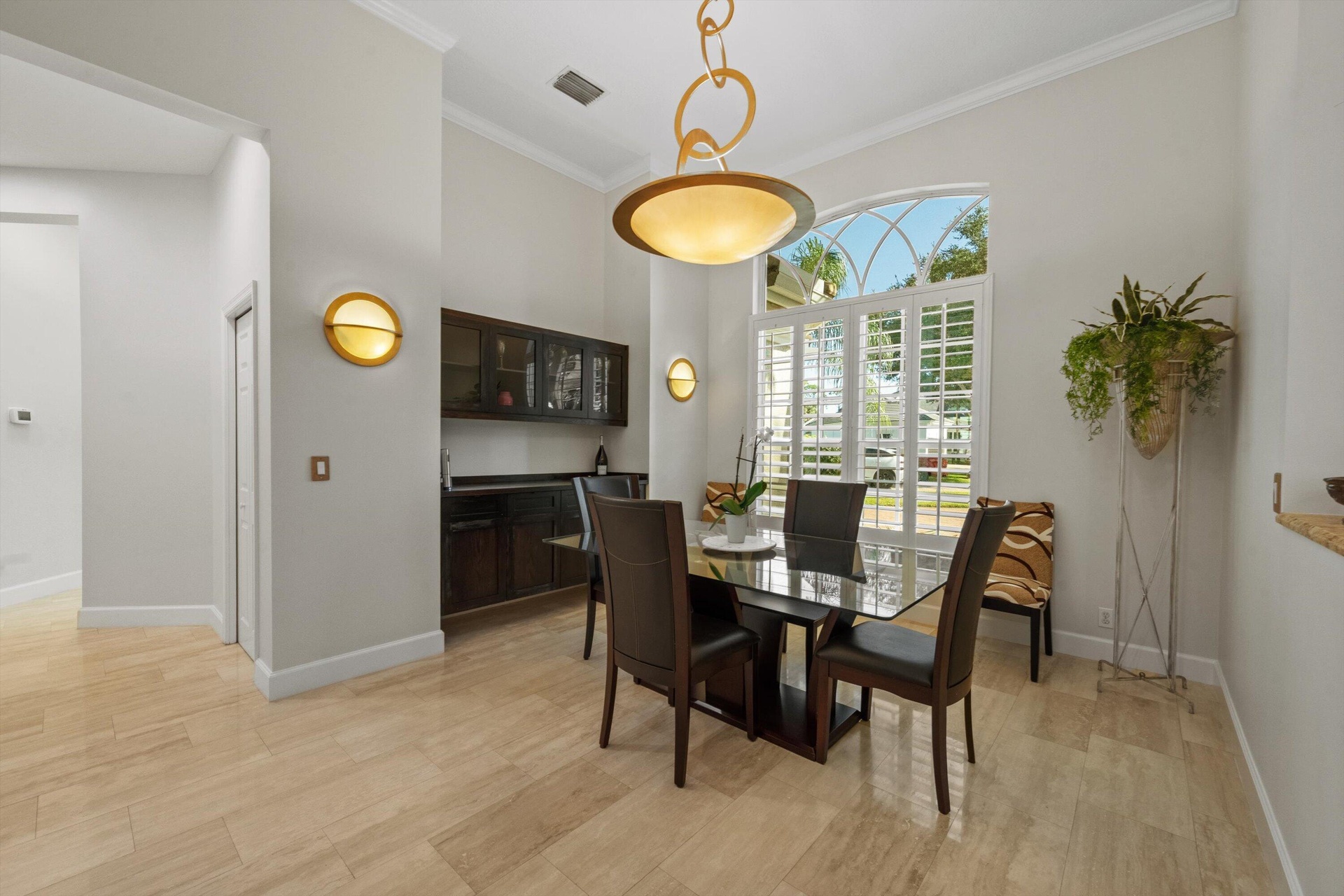 High-ceiling room featuring large arched window with plantation shutters, built-in dark wood cabinetry, polished light-tone tile flooring, and integra