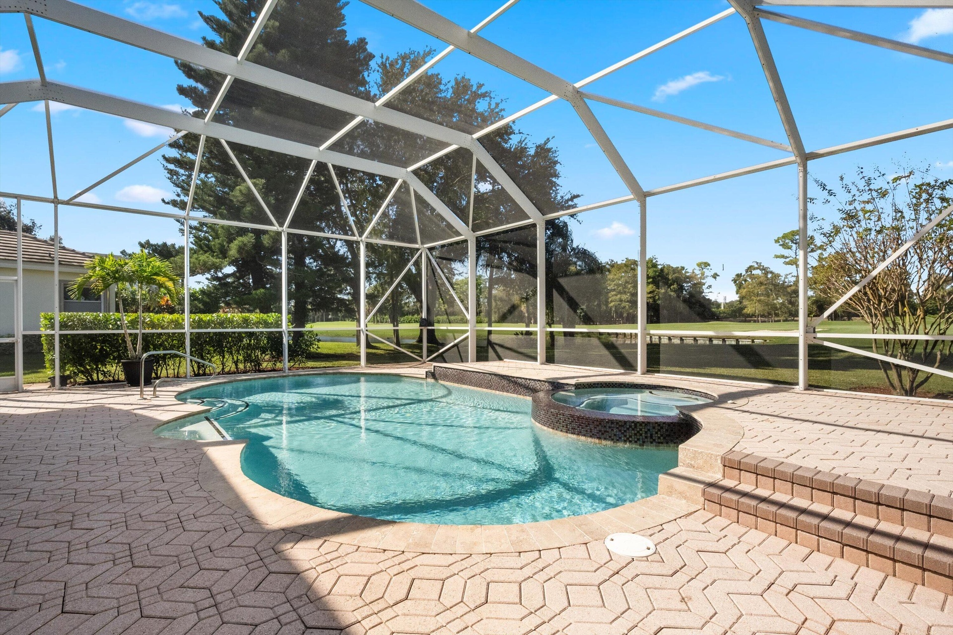 Screen-enclosed pool area featuring a spillover spa, tiled deck, and brick-style pavers