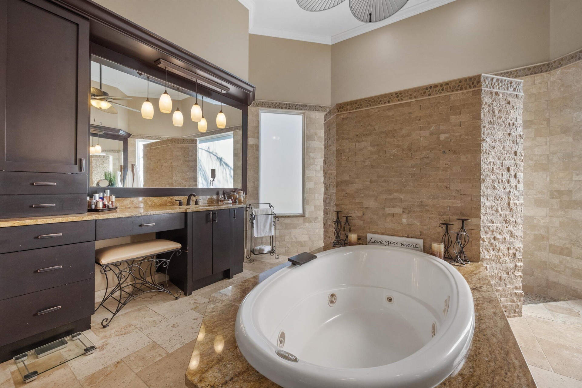 Bathroom featuring a deep soaking tub with a stone-surround deck, stacked stone wall accents, dark wood-finish cabinetry, and a large framed mirror wi