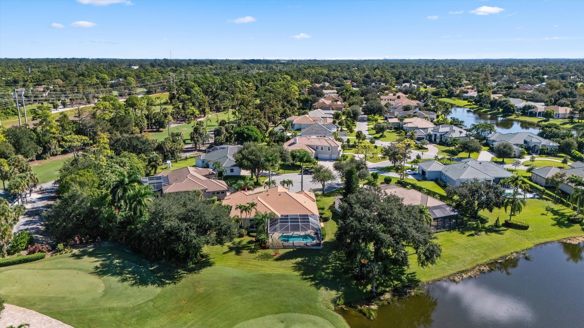 Aerial perspective of a property featuring a screened-in swimming pool, tile roof, and manicured landscaping, situated directly on a golf course fairw