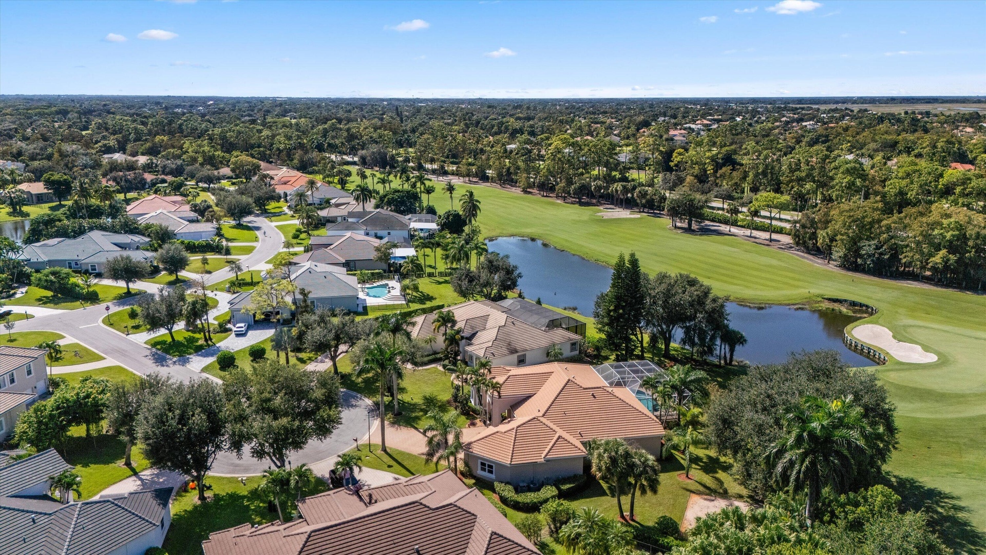 Aerial perspective featuring a multi-hipped roof residence positioned alongside a golf course fairway and a water feature, incorporating mature trees 