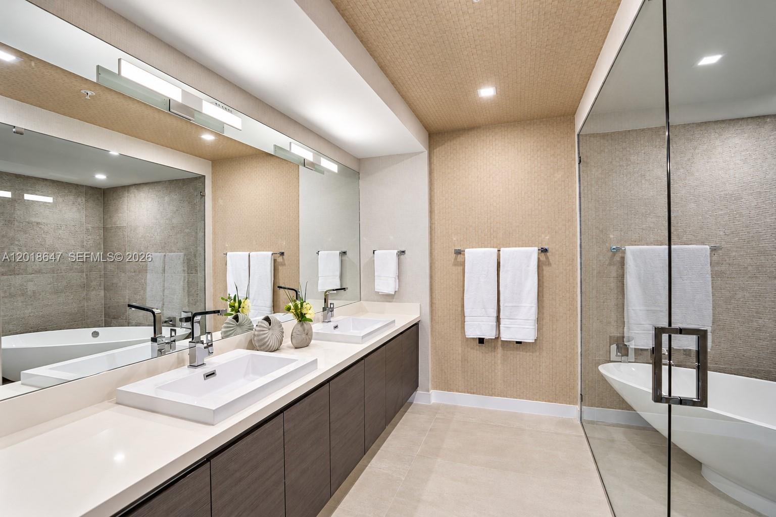 Freestanding soaking tub with wall-mounted faucet, floor-to-ceiling stone tile, walk-in shower with glass enclosure, overhead rain shower head, and bu