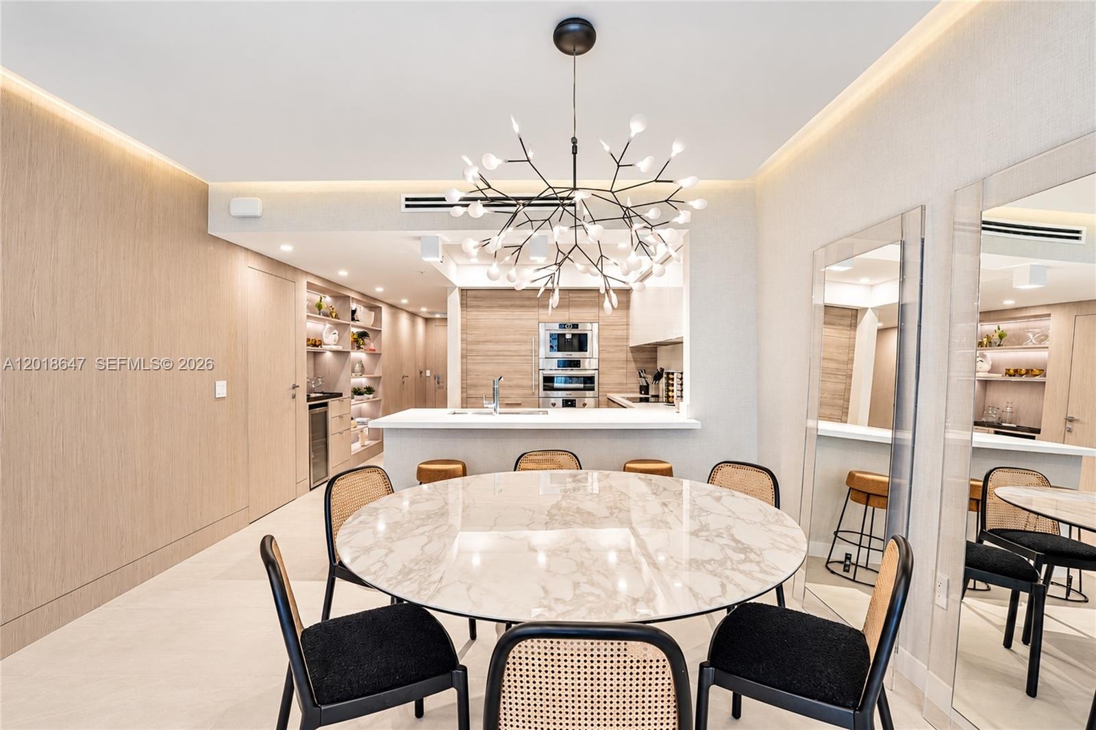 Modern kitchen featuring light wood-finish cabinetry, a white countertop island with an integrated sink, built-in stainless steel appliances, recessed