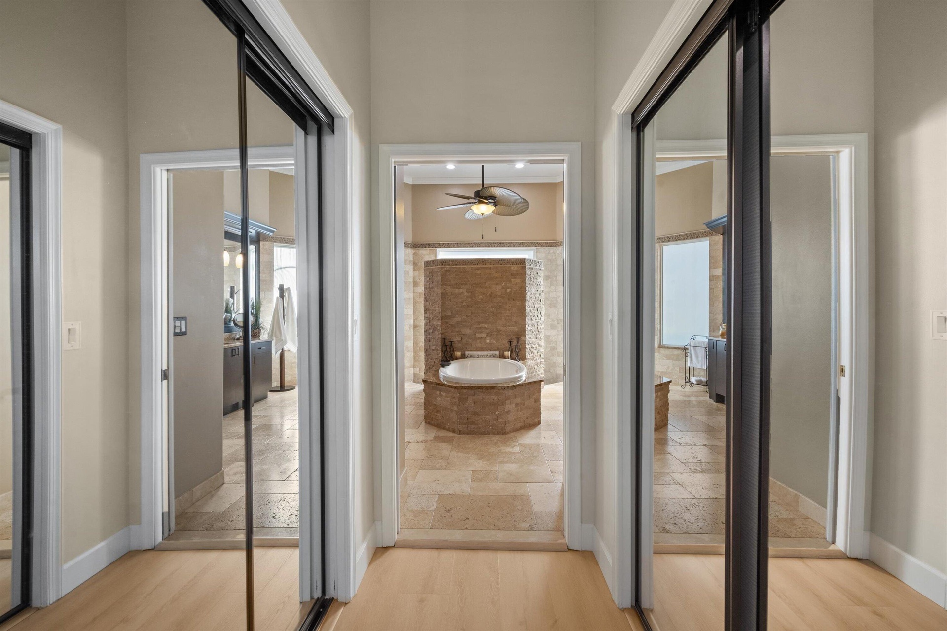 Hallway featuring dual floor-to-ceiling mirrored sliding closet doors, stone-tile flooring, and direct line-of-sight to an inset soaking tub with ston